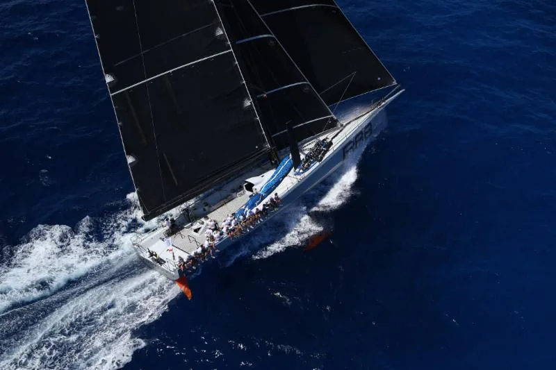 Swan yacht sailing offshore beneath a mountain coastline