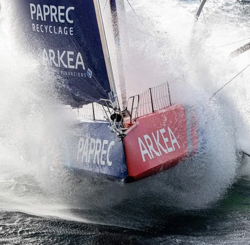 Bow of IMOCA 60 Arkea Paprec bursting through a wave